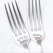 Two silver plate forks with the inscription 'Life is Sweet With You' stamped on them, displayed on a white surface.