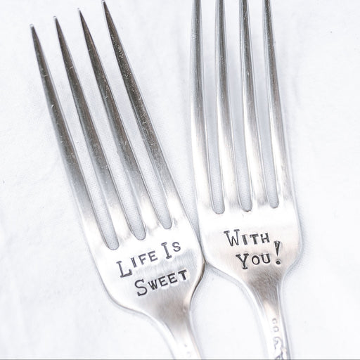 Two silver plate forks with the inscription 'Life is Sweet With You' stamped on them, displayed on a white surface.